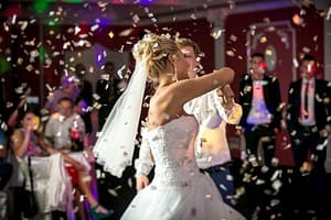 Beautiful blonde bride dancing at restaurant in flying confetti